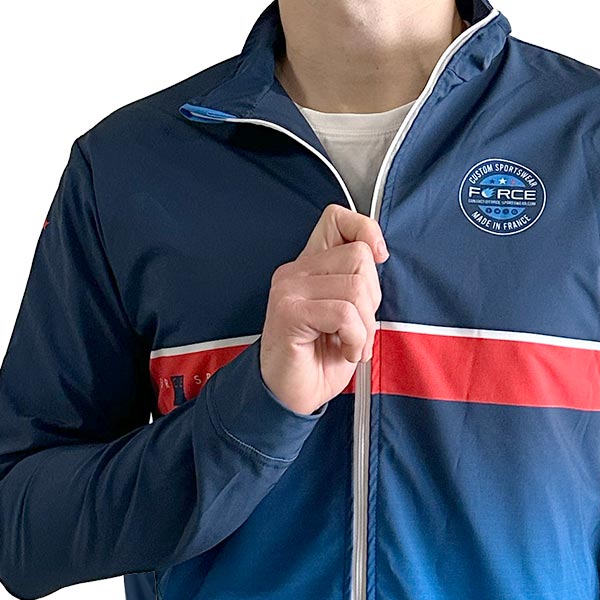 torso of a man wearing a sublimated blue jacket and holding the zipper with his hand