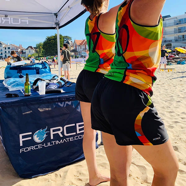 side view of women on beach under a tent wearing colorful jerseys and short black shorts