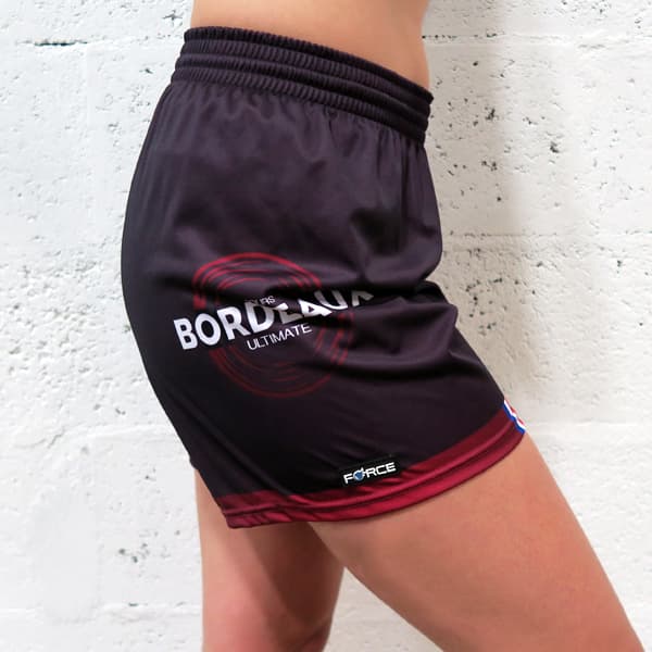 side right view of woman lower body wearing feminine black shorts in front of a white wall